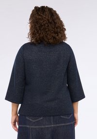Pulover texturat de culoare albastru marin cu mâneci trei sferturi, având un model țesut subtil. Vederea din spate arată o margine dreaptă și un material moale.