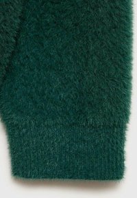 Grön, fluffig stickad tyg med en mjuk textur. Har ett ribbat manschett längst ner, vilket visar upp en tät och fluffig utseende.