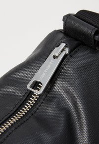 Borsa in tessuto nero con dettaglio della cerniera in metallo argentato, caratterizzata da un tirante esagonale e un attacco per tracolla intrecciato.