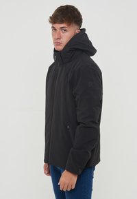 Giacca nera isolante con colletto alto e cappuccio. Presenta tasche laterali con zip e una superficie liscia. Design semplice e moderno.