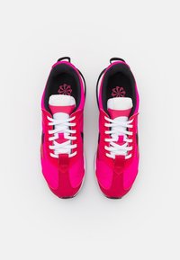 Ljusa rosa sportskor med svarta detaljer. Har vita snören och en dämpad sula, med en elegant och modern design.