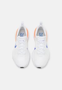 Scarpe sportive bianche con accenti blu e arancioni, superiori texture, stringhe piatte e una linguetta sul tallone.