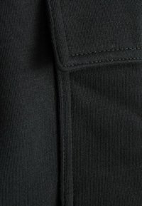 Schwarzer Stoff mit geripptem Muster; verfügt über einen gefalteten Umschlag mit sichtbaren Nähten und einer glatten Oberfläche neben einer Naht.