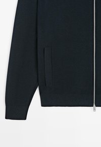 Dark navy zip-up sweater made of textured knit fabric. Features a side pocket and silver-toned zipper for closure.