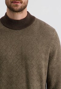 Braun gemusterter Pullover mit einem hohen Rippkragen. Die Textur zeigt ein Rippmuster mit wechselnden Linien, die einen gewebten Effekt erzeugen.
