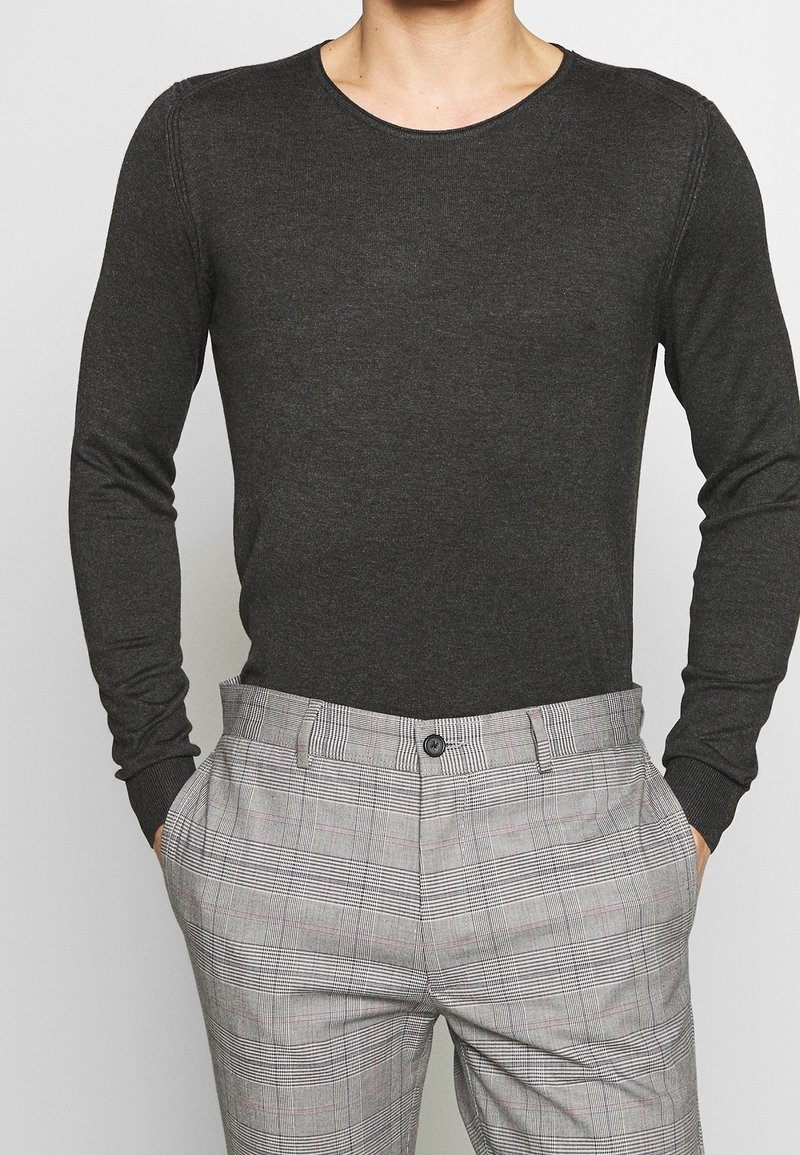 Long-sleeve, dark gray cotton shirt with a round neckline, paired with gray plaid trousers featuring black and pink lines and side pockets.