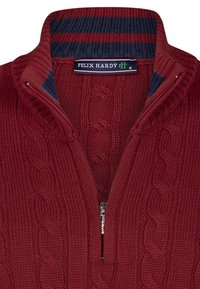Czerwony sweter dziany z kołnierzem na zamek, z wzorami w warkocze i granatowym prążkowanym wnętrzem kołnierza. Etykieta z napisem "FELIX HARDY M."