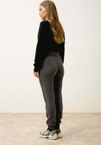 Šedé tepláky s přiléhavým pasem a bočními pruhy, doplněné černými teniskami s šedobílým designem. Viditelná textura z vlněné směsi.