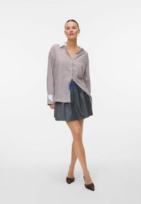 Chemise à rayures rouges claires et blanches, associée à une jupe gris foncé avec un cordon bleu. Des chaussures à talons hauts complètent le look.