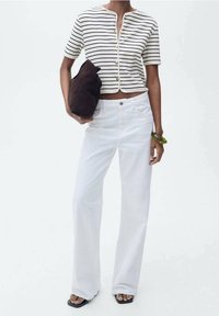 Haut à manches courtes rayé crème et marine, boutonné, associé à un jean blanc évasé. Sac pochette marron et bracelet vert complètent le look.