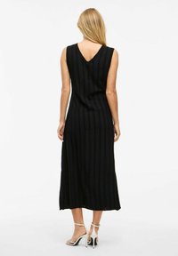 Abito nero senza maniche con scollo a V e righe verticali, con un orlo di lunghezza intermedia. Texture liscia. Indossato con sandali con cinturino.