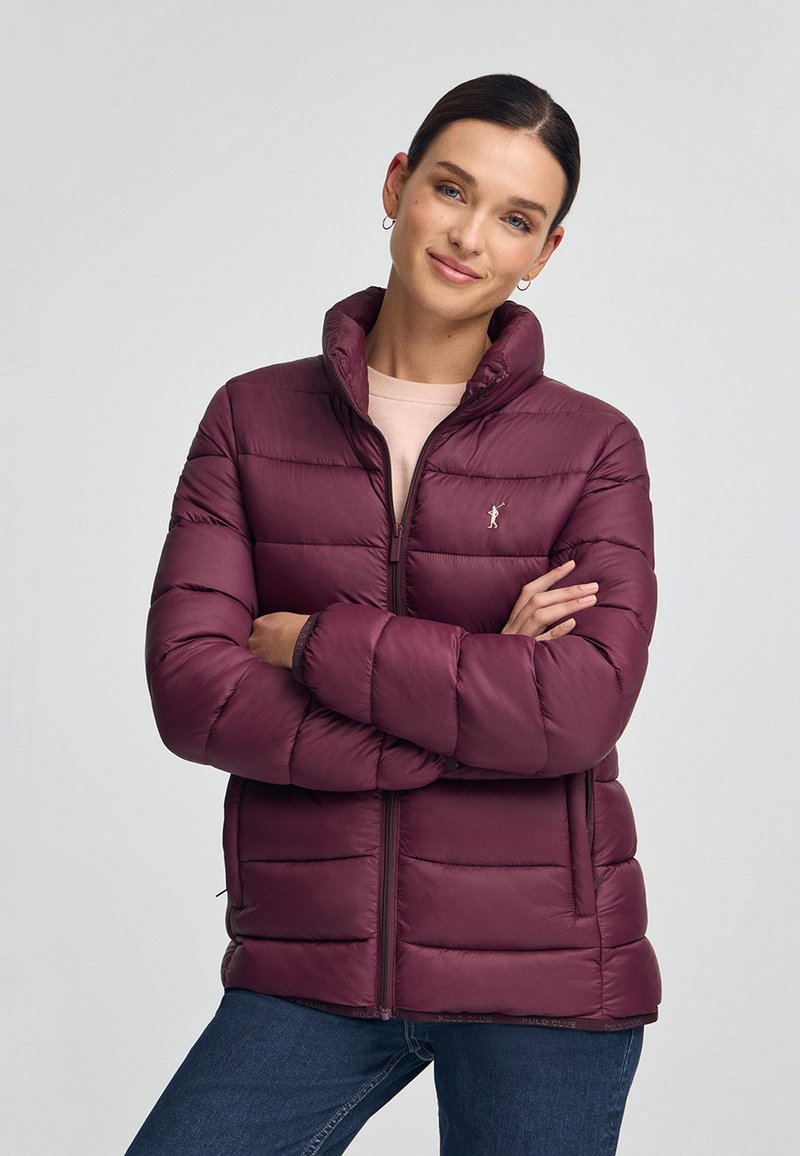 Bordeauxfärgad puffjacka med hög krage, dragkedja och elastiska ärmslut. Utrustad med horisontell quiltad design och logotypbroderi på bröstet.