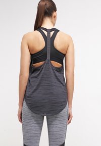 Donkergrijze sporttanktop met racerback ontwerp, voorzien van gestructureerde stof en uitsnijdingen bij de schouders, gecombineerd met gestreepte leggings.