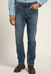 Modré denimové džíny s přiléhavým střihem; mají pět kapes, zip a jemné kamenové umytí. Hnědé kožené boty.