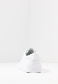 Vitsneaker i läder med rundad design, flat sula och minimalistisk märkning på hälen och sidan. Slät yta, inga synliga mönster.