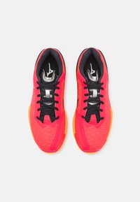 Des chaussures de sport rouges et orange avec des lacets noirs, une tige en maille, une semelle en caoutchouc et des accents argentés sur la languette et sur les côtés.
