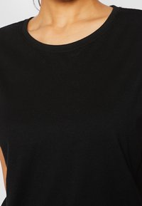 Černé bavlněné tričko s kulatým výstřihem a krátkými rukávy. Hladká textura a minimální švy jsou viditelné. Jednoduchý design bez vzorů.