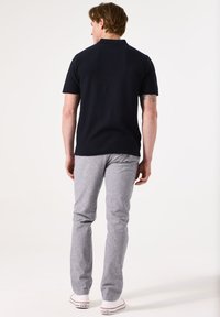 Marineblauw polo-shirt met korte mouwen van textiel, gecombineerd met lichtgrijze broek. Schoenen hebben witte zolen met rode accenten.