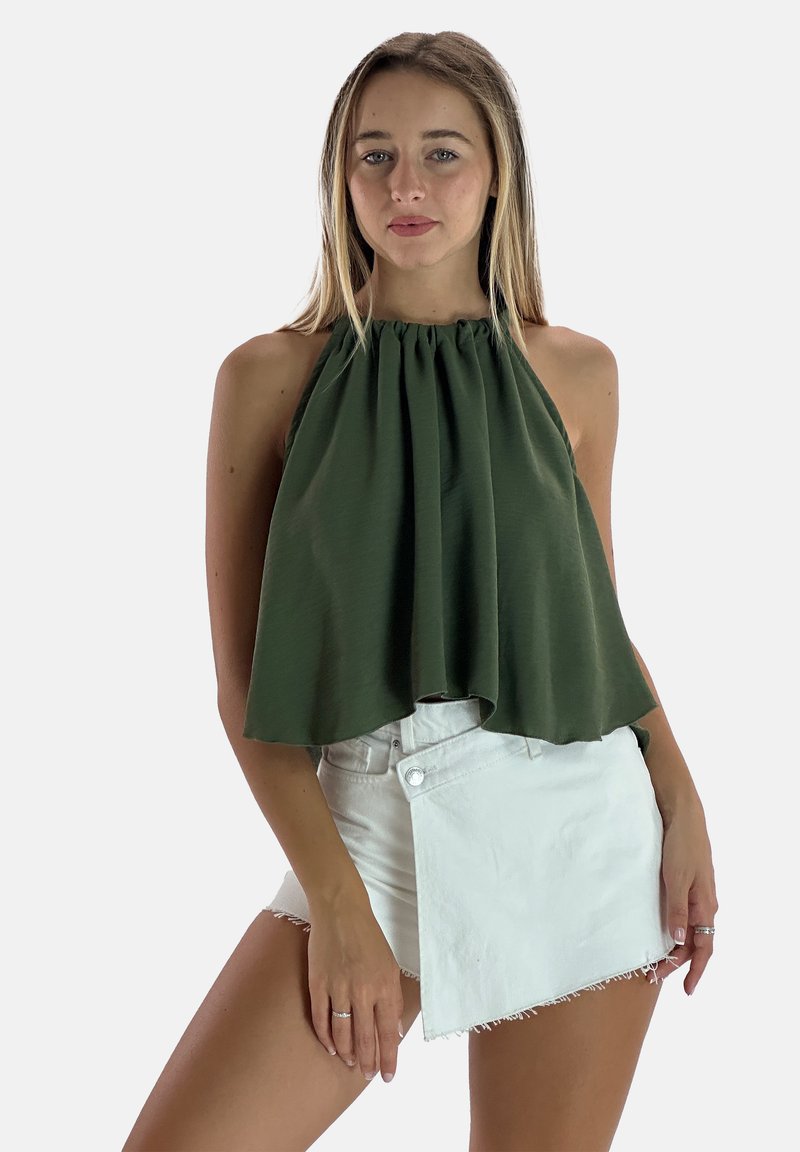 Top halter verde oliva con scollatura arricciata e vestibilità ampia, abbinato a pantaloni corti bianchi con taglio asimmetrico e orli sfrangiati.