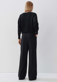 Schwarzer Pullover mit lockerem Schnitt und Rundhalsausschnitt, kombiniert mit hoch taillierten schwarzen weiten Hosen mit Seitentaschen.