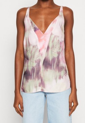 Mujer con una blusa sin mangas y cuello en V con un patrón floral abstracto en rosa, morado y verde, combinada con vaqueros azul claro.