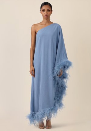 Woman wearing a floor-length, one-shoulder light blue dress with feather trim along the hem and one sleeve, standing against a neutral background.