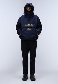 Tmavě modrá mikina s zipem, obsahující přední kapsu, logo a malou norskou vlajku. Nosič má na sobě černé kalhoty a boty.