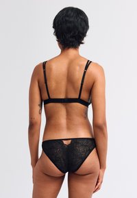 Schwarzes BH- und Spitzenstring-Set mit verstellbaren Trägern, das ein strukturiertes florales Muster und ein Schlüssellochdetail auf der Rückseite des Strings aufweist.