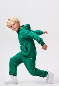 Groene hoodie en sweatpants set gemaakt van zachte stof. Beschikt over een kangoeroezak, geribde manchetten en witte hoge sneakers.