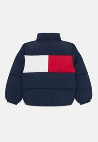 Abrigo acolchado azul marino con un cuello alto, que presenta un diseño de bloques rectangulares blancos y rojos en la parte trasera. Textura suave y acolchada.