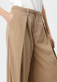Beige wide-leg trousers with a high waist, pleats, and belt loops. Fabric has a smooth texture, featuring side pockets and a tailored fit.