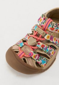 Tan-washable sandaalit, joissa on värikkäät kukkakuosiset hihnat, säädettävät sulut, leikattu muotoilu ja teksturoitu ruskea kumipohja.