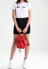 Vit t-shirt med svarta ögonfransar, högmidjade mörka short, röd läderryggsäck och vita ankelskor. Enkelt och modernt outfit.