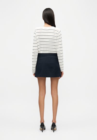 Λευκή και ναυτική ριγέ μπλούζα με μακριά μανίκια συνδυασμένη με ναυτική μίνι φούστα. Μαύρα παπούτσια με ψηλό τακούνι ολοκληρώνουν το look. Απλός και εφαρμοστός σχεδιασμός.