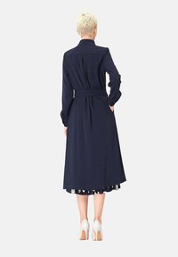 Robe longue bleu marine à manches longues, avec un col et une ceinture à nouer à la taille, présentant un ourlet plissé et une jupe fluide.