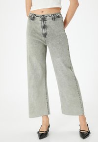 Lichtgrijze wijde jeans met een vervaagd ontwerp, hoge taille, vijf zakken en een rauwe zoom. Gecombineerd met zwarte laarzen van patenterend leer.