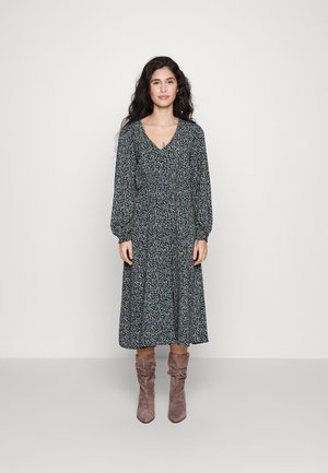 Long-sleeve dress in dark blue fabric with a floral pattern, V-neckline, and gathered waist. Paired with taupe slouchy ankle boots.