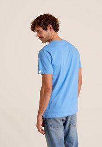 Lichtblauwe katoenen t-shirt met korte mouwen, ronde hals en een klein logo-label op de linker mouw, gecombineerd met spijkerbroek.