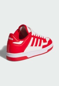 Crvene i bijele Adidas tenisice imaju glatku sintetičku gornjište, sa tri bijele pruge i teksturiranim gumom potplatom. Perice su bijele.