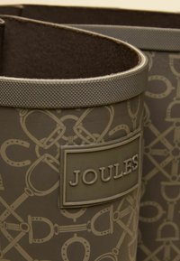 Tmavohnedá nádoba vyrobená z odolného materiálu, s textúrovaným okrajom a jazdeckým vzorom, s výrazným logom "JOULES".