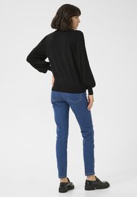 Maglione nero con maniche a sbuffo e dettagli in perline testurizzate; abbinato a jeans slim blu e scarpe con plateau nere.