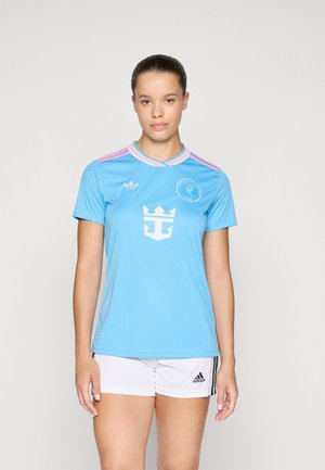 Light blue soccer jersey with pink accents, featuring a round collar, striped pattern, and emblem on the chest. Paired with white shorts.