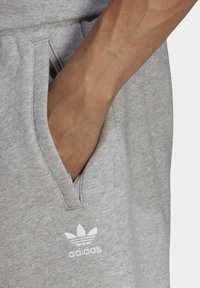 Tessuto grigio di una felpa con un taschino visibile, con un logo Adidas ricamato bianco e un materiale morbido e testurizzato.