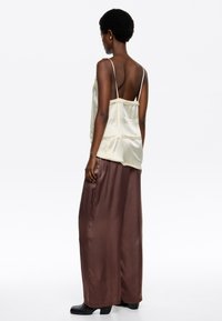 Camisón de satén en crema claro con tirantes finos, combinado con pantalones de pierna ancha de satén marrón oscuro de talle alto y botas negras de tacón.