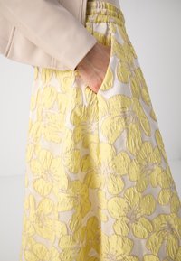Jupe jaune brodée de fleurs sur fond crème, dotée d'une taille élastique froncée et d'une poche latérale. Texture lisse.