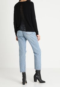 Schwarzer Pullover mit Spitzenpaneel auf dem Rücken, kombiniert mit leicht blauen, verwaschenen Jeans und schwarzen, hochhackigen Stiefeletten.
