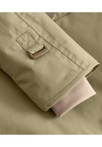 Khaki jakke mansjett med en jevn tekstur, med en brun metallspenne og myk beige innerforing. Synlig søm detalj.