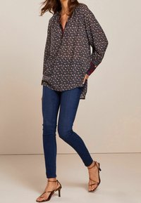 Mørk blomsterprint blouse med en afslappet pasform, knaplukning ved halsen og lange ærmer. Sammen med tætsiddende mørke jeans og brune stiletter med remme.