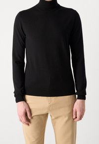 Schwarzer Rollkragenpullover mit langen Ärmeln, gerippten Bündchen und Saum. Glatte Textur mit figurbetontem Design, getragen mit hellen Hosen.