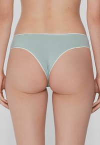 Helleblauer Baumwoll-Mix-Tanga mit gewelltem weißen Abschluss. Verfügt über einen tief geschnittenen Bund und minimalen Rückendeckung. Glatte Textur.